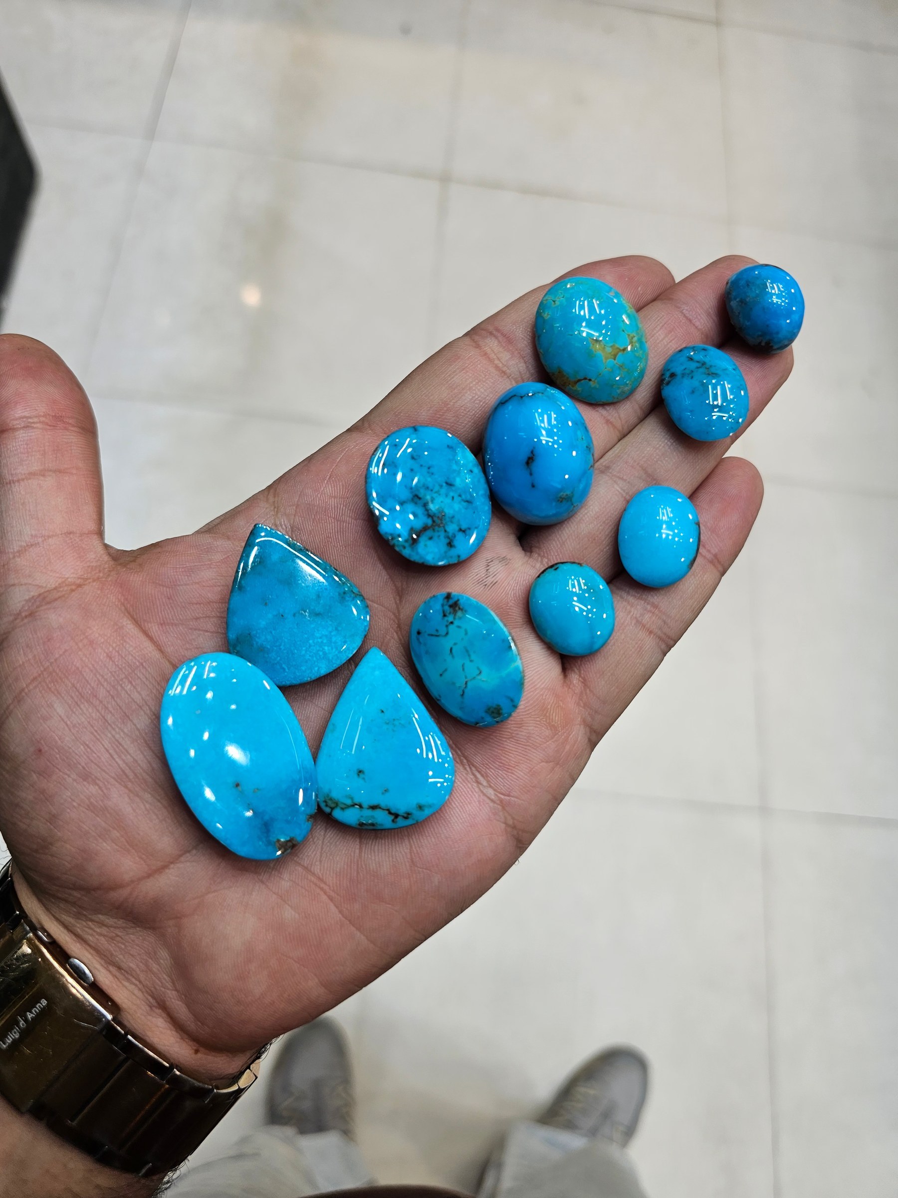 A hand holds a group of polished oval turquoise cabochons in solid bright and medium blue.