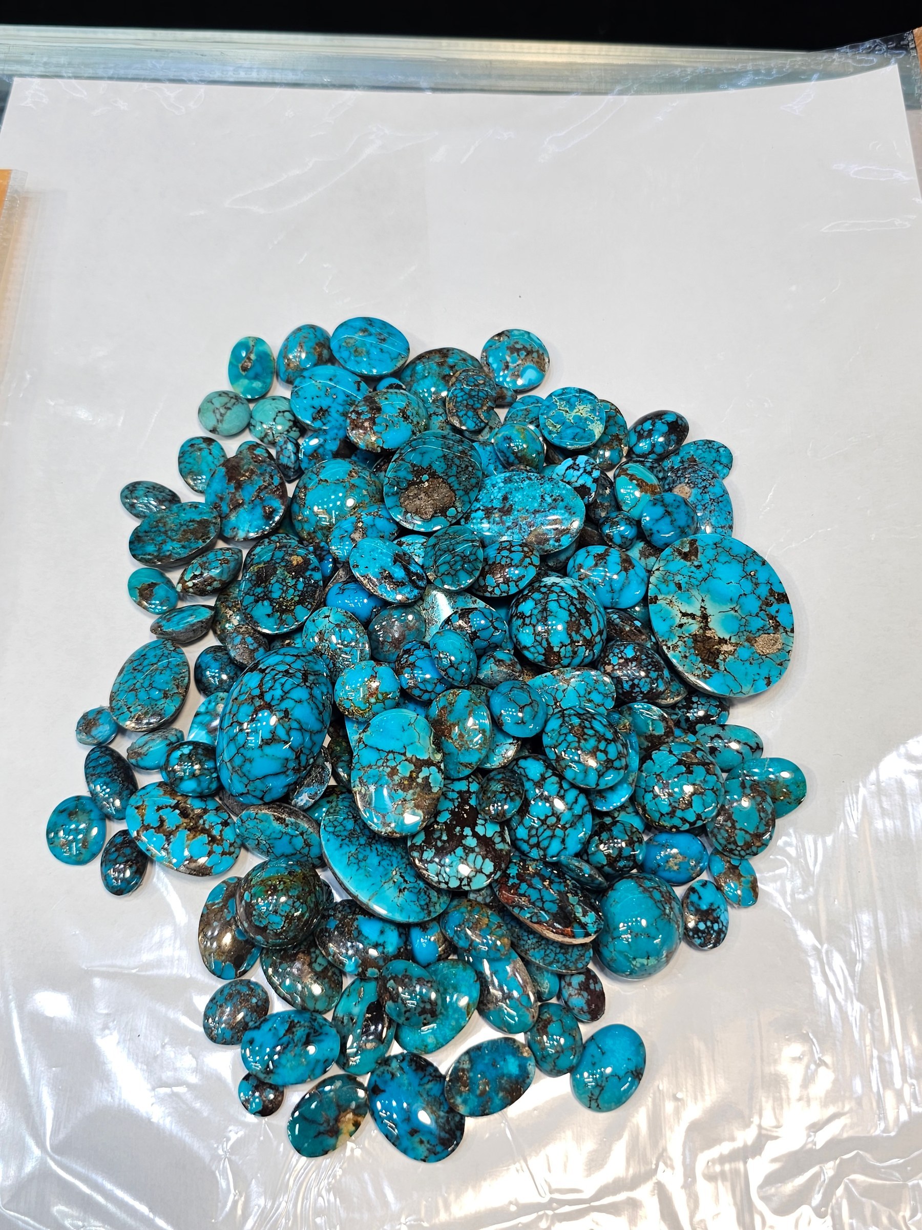 The same mound of loose blue turquoise cabochons seen from a slightly different angle on a white sheet.