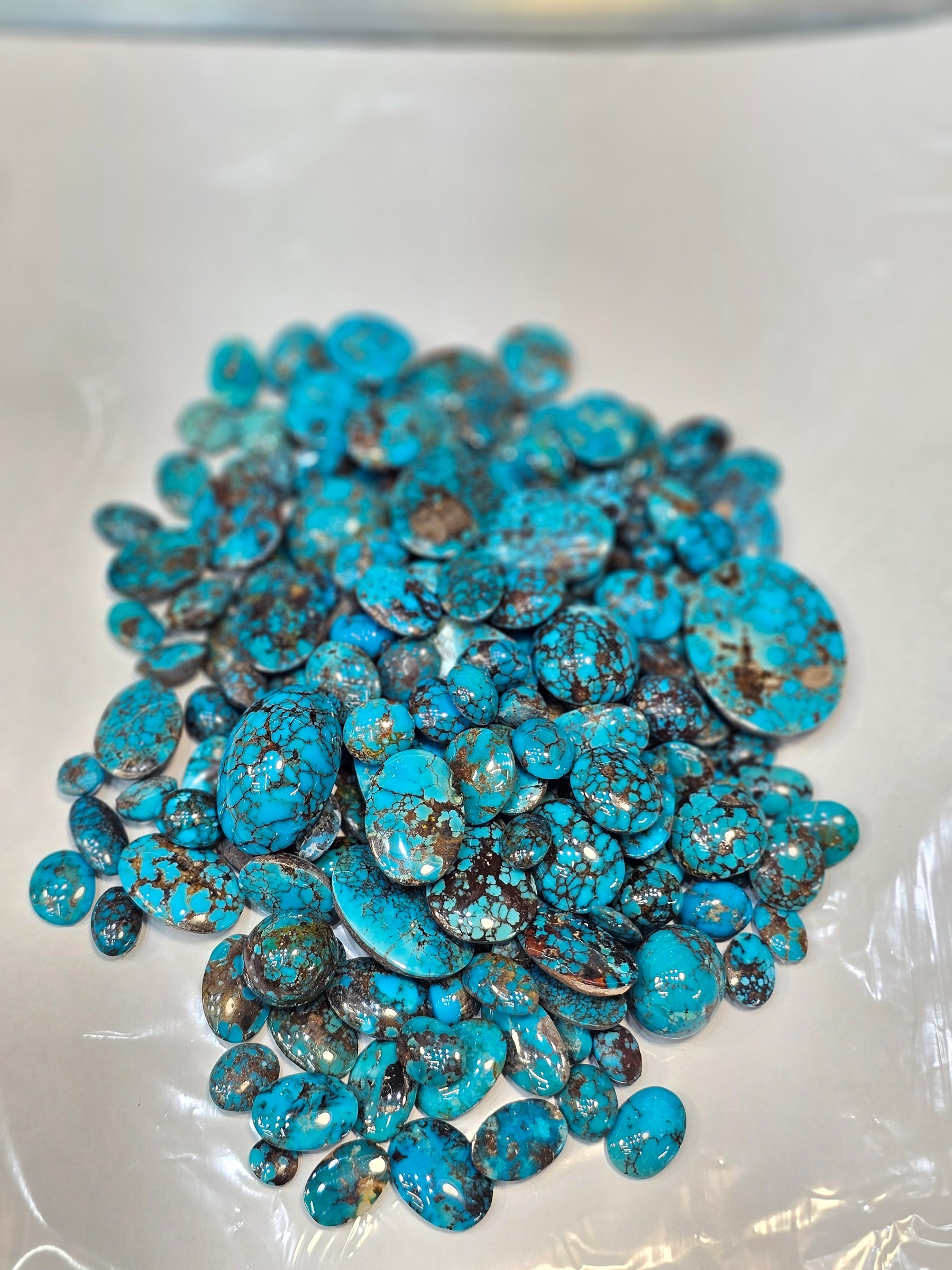 The same parcel of loose blue turquoise cabochons on a white sheet, viewed from further above.