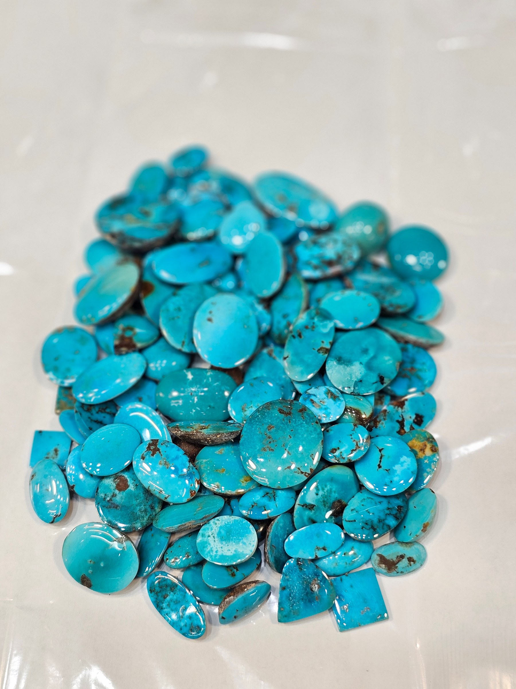 The same pile of loose brighter blue turquoise cabochons viewed from a lower angle on a white sheet.