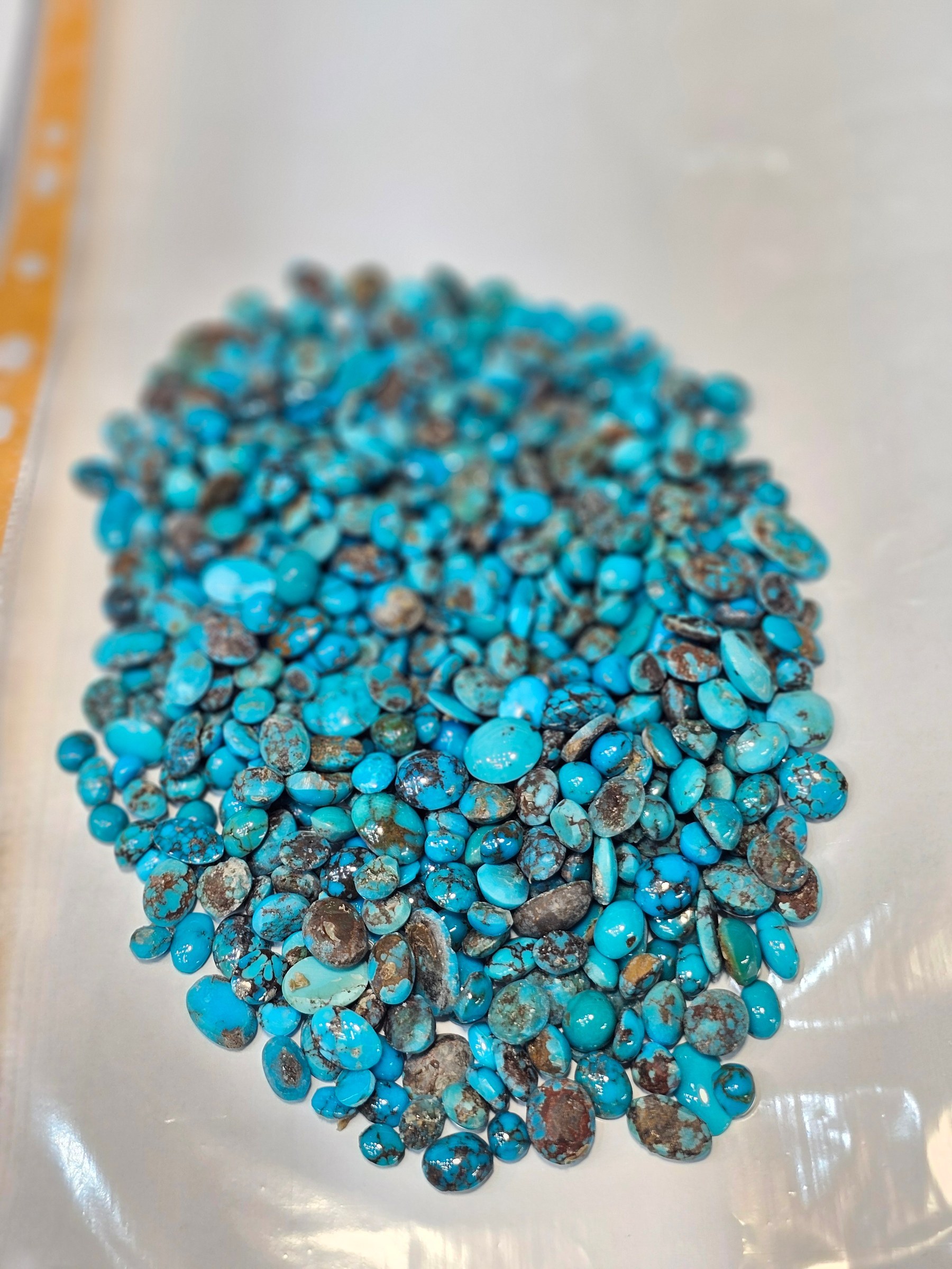 The same parcel of loose blue turquoise cabochons on a white sheet, viewed from further away.