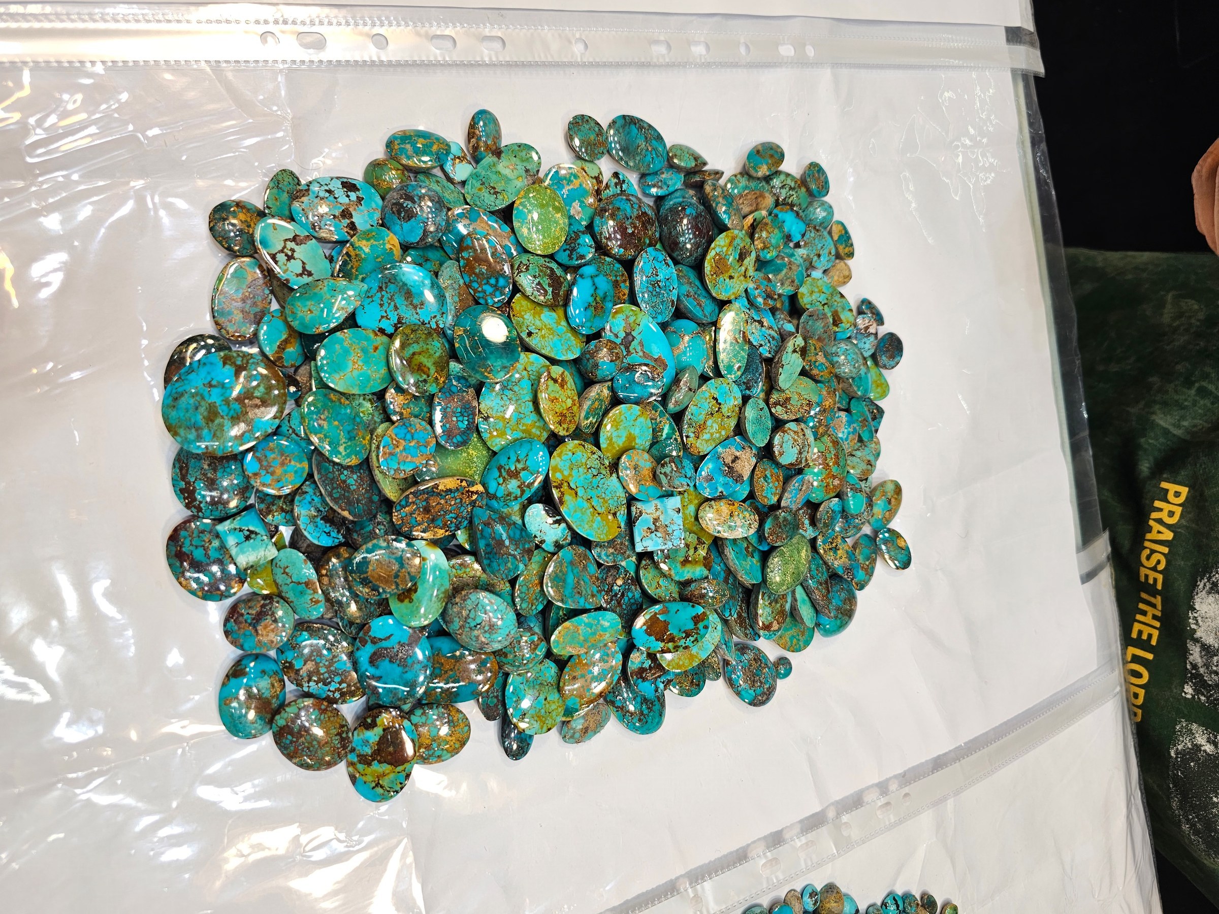 The same green-brown pile of loose turquoise cabochons photographed on a clear plastic sheet.