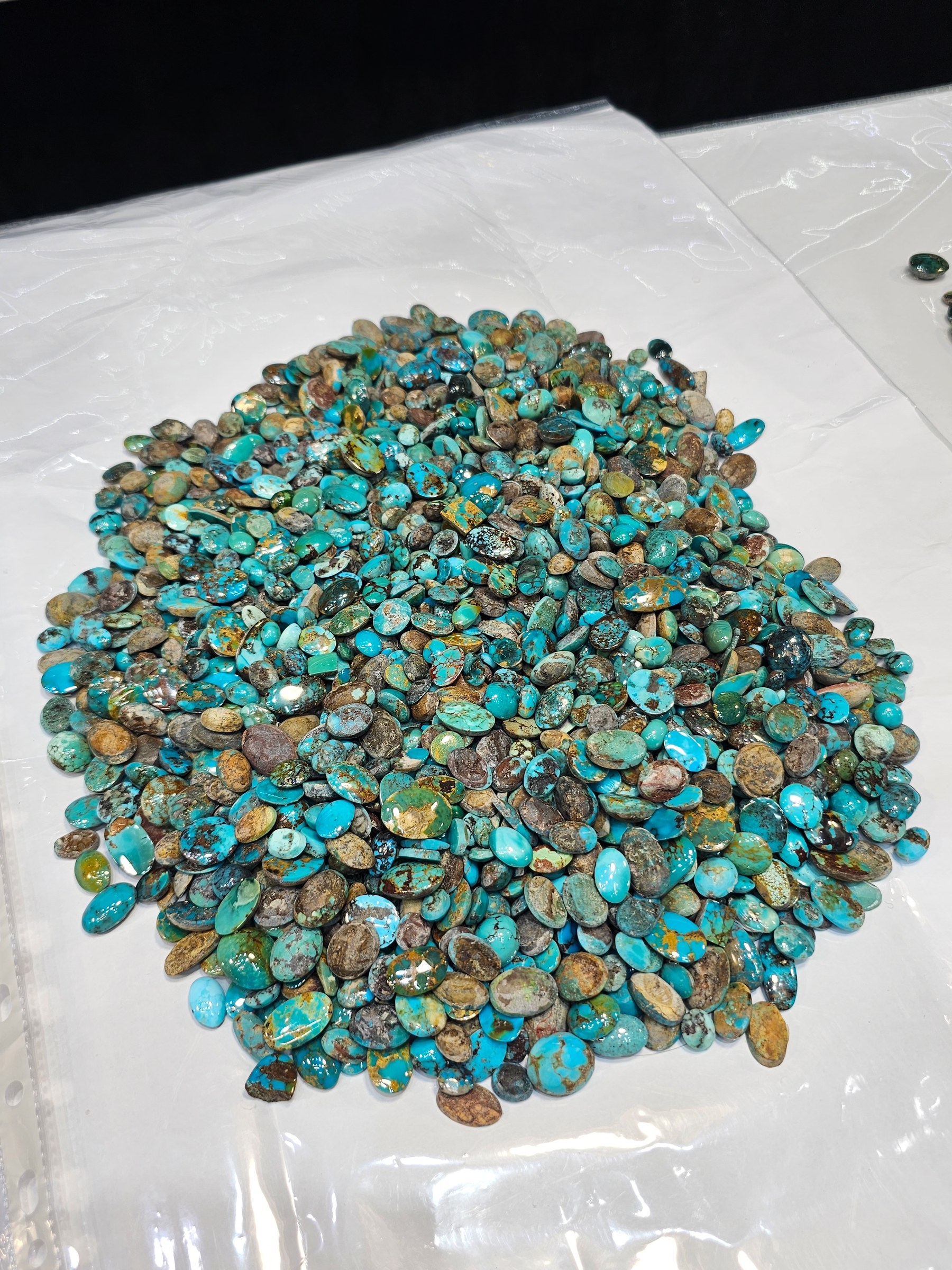 The same green-brown parcel of loose turquoise cabochons spread across a white sheet.