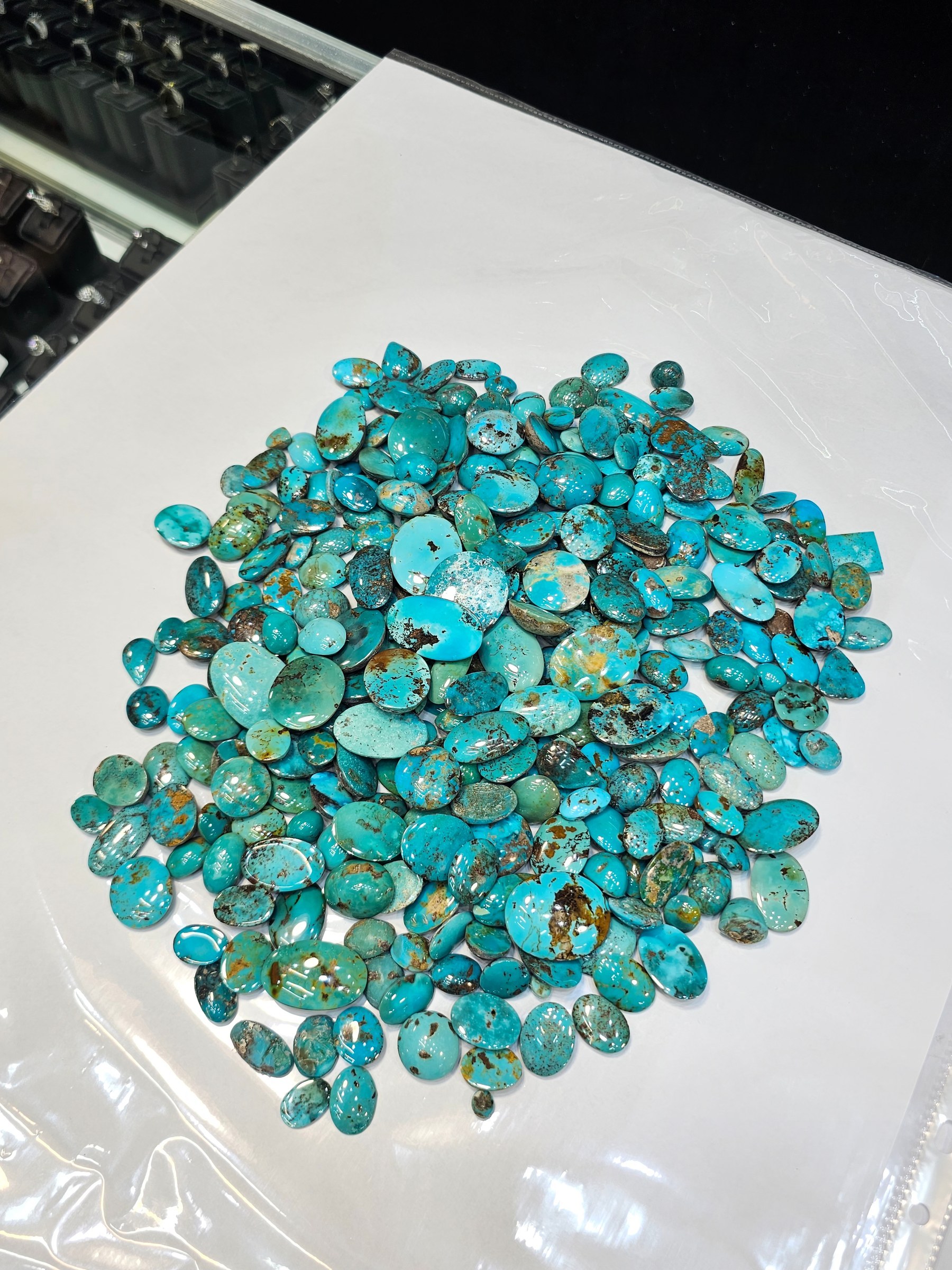 The same green-brown parcel of loose turquoise cabochons on a white sheet beside a work surface.