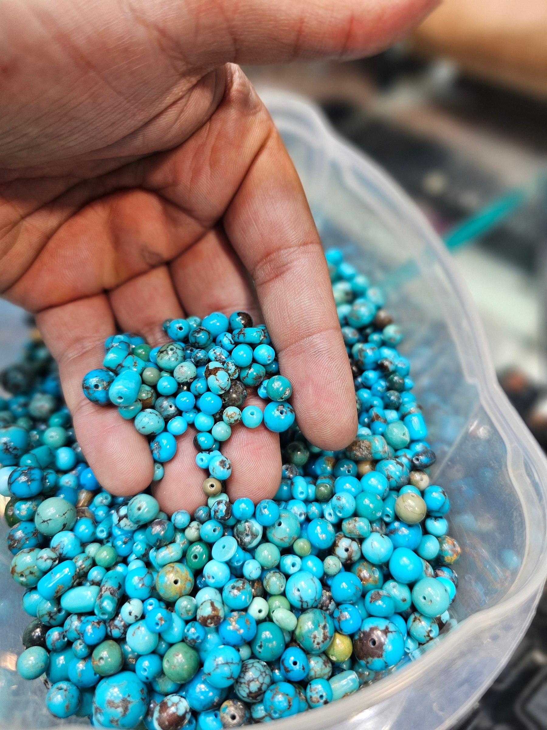 A hand holds a handful of small round drilled turquoise beads in bright blue with green matrix.