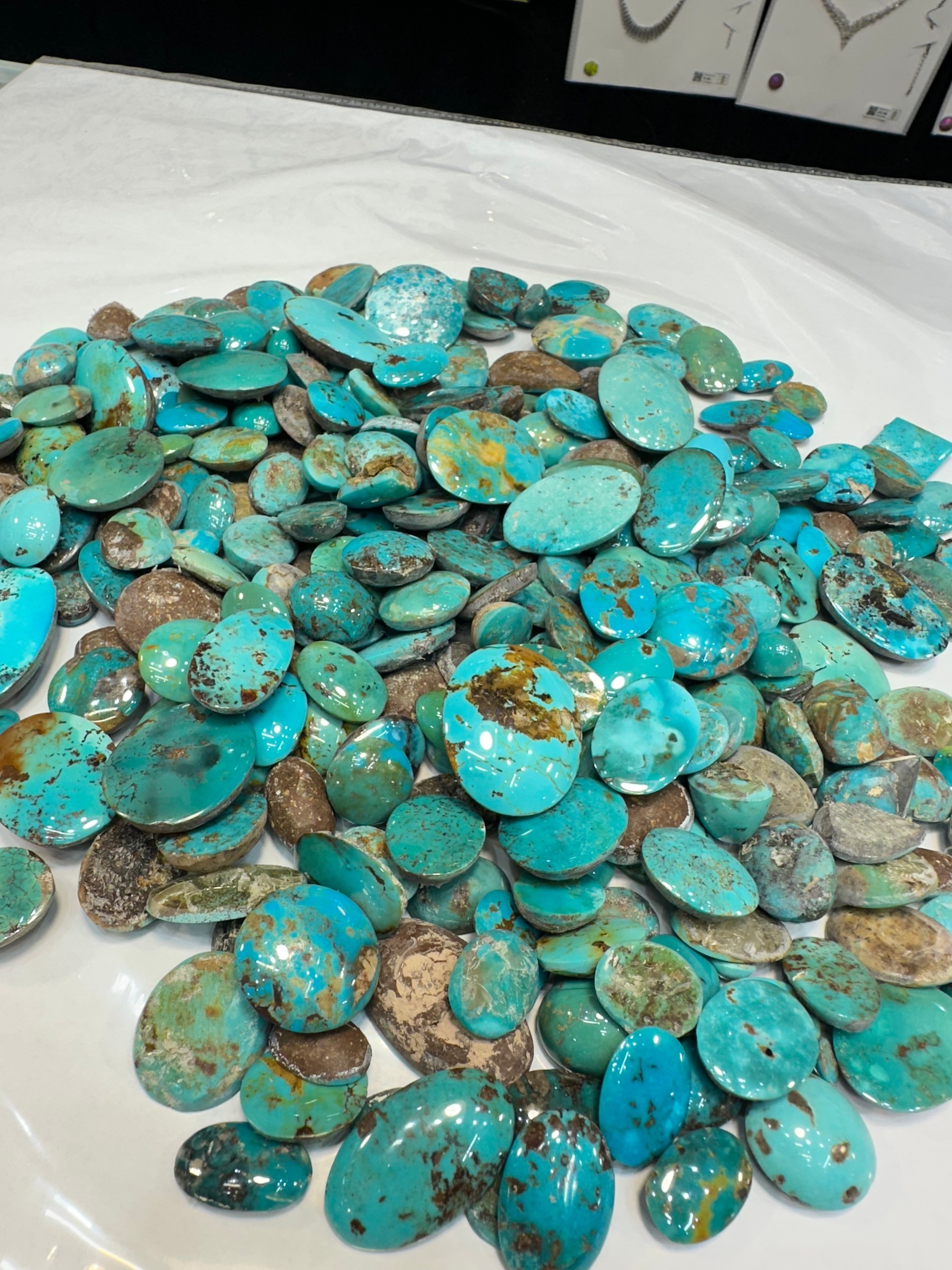 A spread of loose polished turquoise cabochons in blue and green-brown tones on a white sheet.