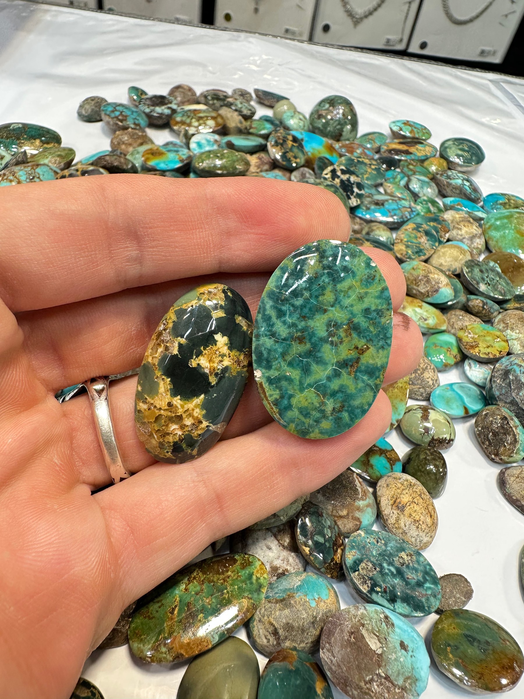 A hand holds two polished turquoise cabochons in green with dark matrix above a parcel.