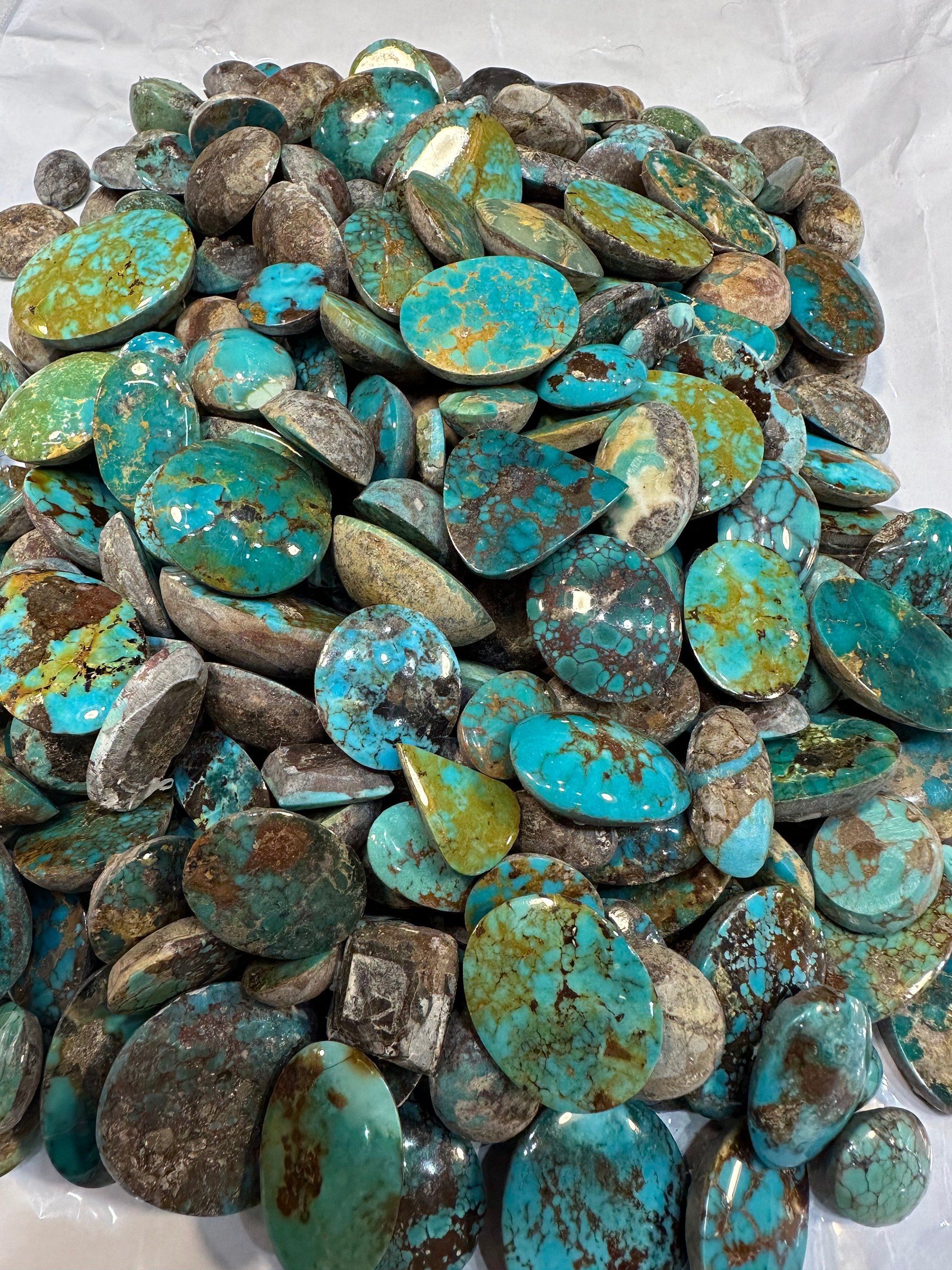 A closer spread of loose polished turquoise cabochons in green-brown with heavy matrix.