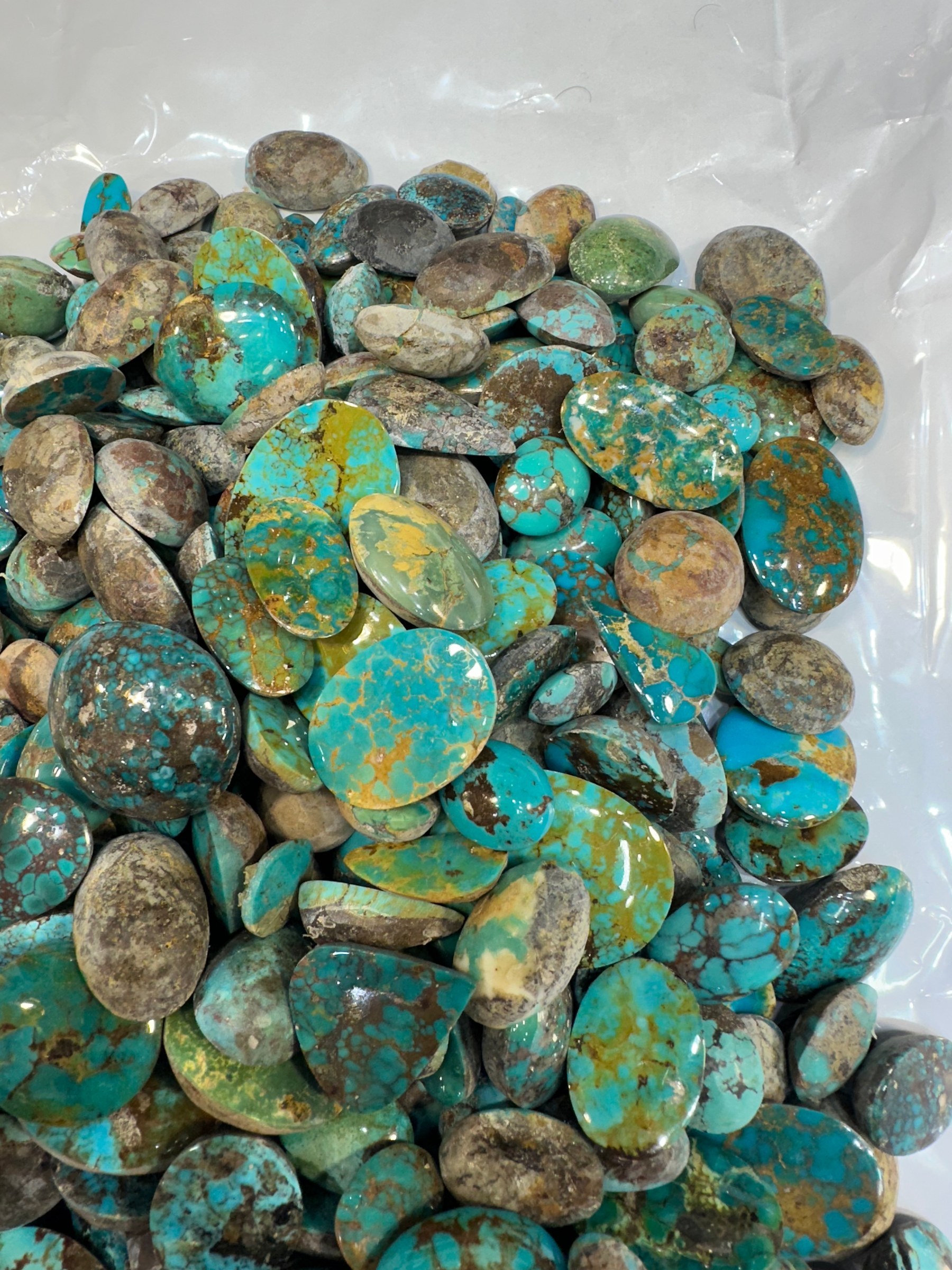 A spread of loose polished turquoise cabochons in blue and green-brown tones on a white sheet.